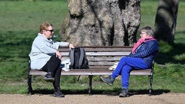 people sit at either end of a park bench as they talk in Clapham Common in south London on March 24, 2020 after Britain's government ordered a lockdown to slow the spread of the novel coronavirus. (AFP)