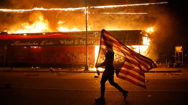A protester carries a U.S. flag upside down, a sign of distress, next to a burning building Thursday, May 28, 2020, in Minneapolis. (AP)