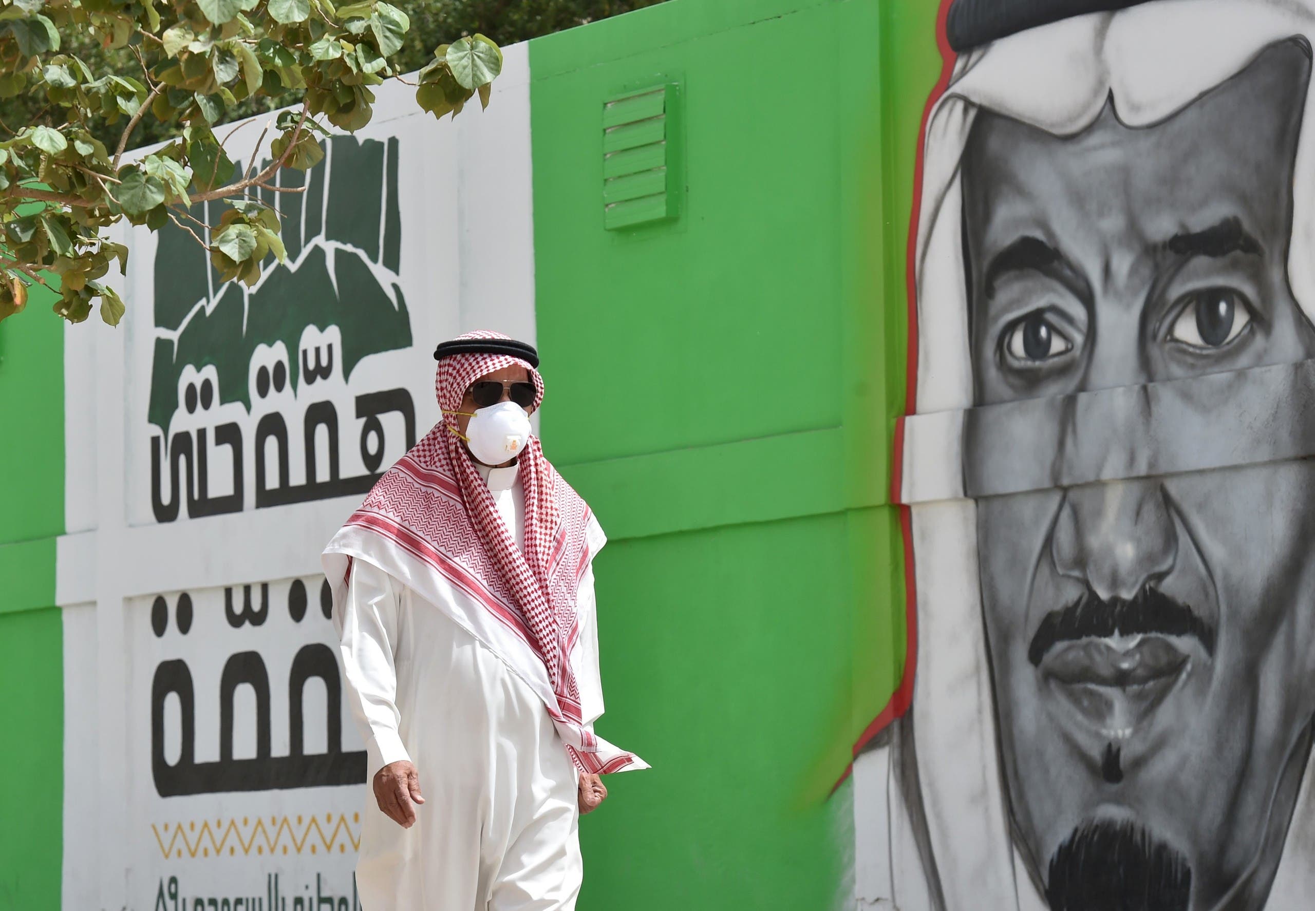 A Saudi man walks past a mural showing the face of King Salman bin Abdulaziz, in Riyadh on March 15, 2020. (AFP)
