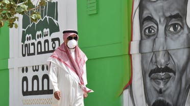A Saudi man walks past a mural showing the face of King Salman bin Abdulaziz, in Riyadh on March 15, 2020. (AFP)