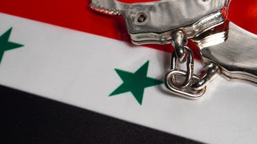 Handcuffs with hand on Syria flag stock photo