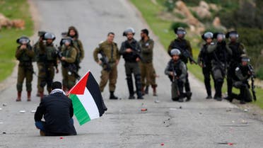 A Palestinian demonstrator holds a national flag in front of Israeli forces in Jordan Valley in the West Bank on Feb. 25, 2020. (AP)