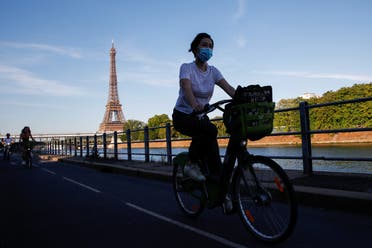 A woman wearing a protective mask rides a bicycle near the Eiffel Tower during a warm and sunny day in Paris as a heatwave hits France, June 24, 2020. (Reuters)