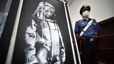 A policeman stands guard near a piece of art attributed to Banksy, that was stolen at the Bataclan in Paris in 2019, and found in Italy, ahead of a press conference in L'Aquila on June 11, 2020. (AFP)