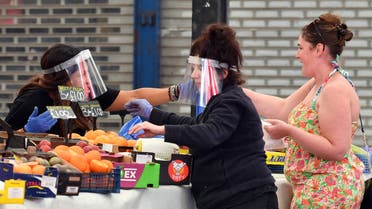 raders wearing PPE (personal protective equipment), including gloves and a visor as a precautionary measure against COVID-19, serve customers at their fruit and vegetable stall at Leicester Market in Leicester. (AFP)