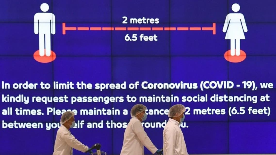 Employees at Dubai International Airport, walk past a poster reminding passengers to keep a safe distance from each other, after the resumption of scheduled operations by Emirates airline, amid the coronavirus pandemic, on May 22, 2020. (AFP)
