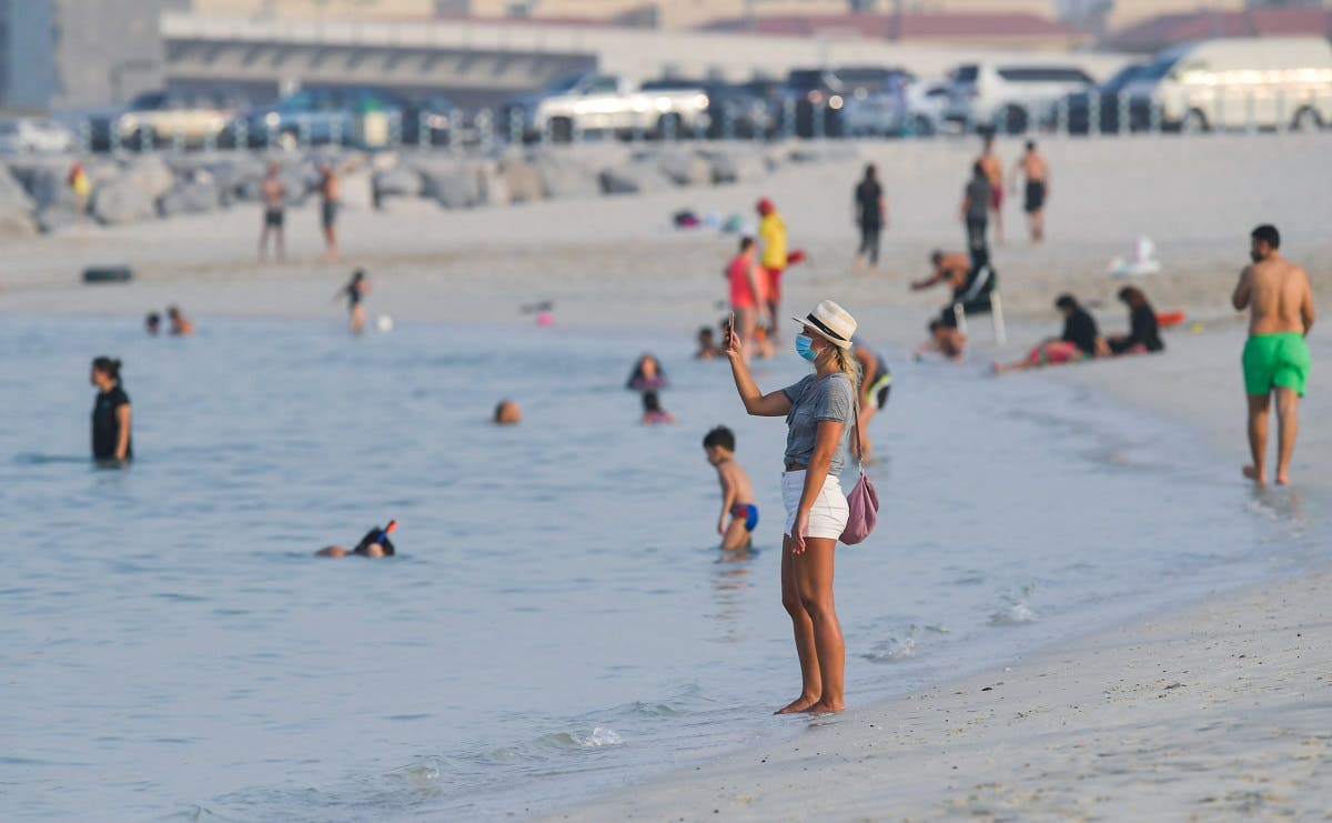 A woman, clad in mask due to the COVID-19 coronavirus pandemic, uses her phone to take a picture along a beach in Dubai. (File photo: AFP)