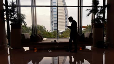 A mask-clad staff member of the Jumeirah al-Naseem hotel walks past a window while behind him is seen the Burj Al Arab hotel. (Reuters)