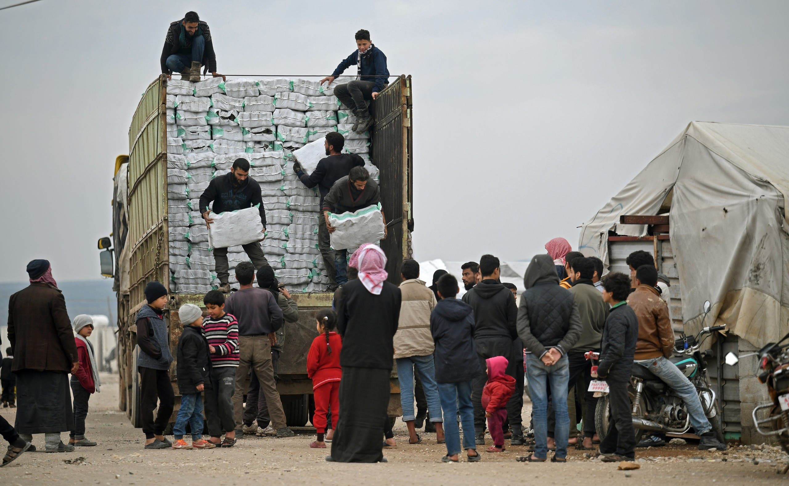 Displaced Syrians queue to receive humanitarian aid, consisting of heating material and drinking water, at a camp in the town of Mehmediye, near the town of Deir al-Ballut along the border with Turkey, on February 21, 2020. 