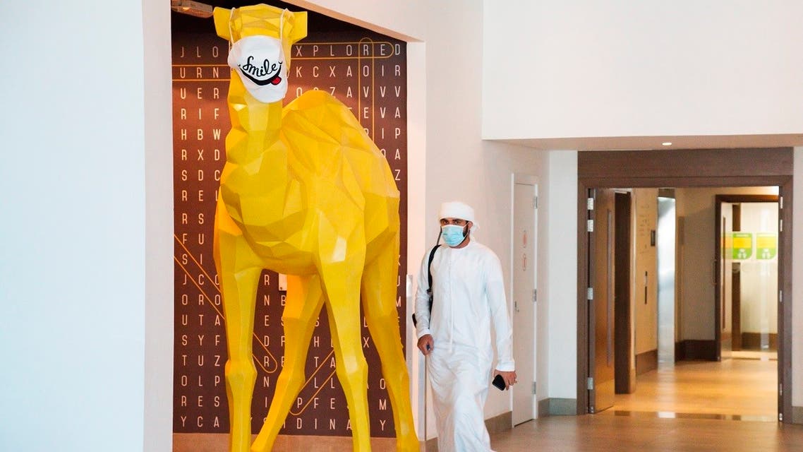 An Emirati wearing a face mask due to the coronavirus pandemic walks past a camel statue decorated with a face mask at the Rove City Centre Hotel in Dubai. (AP)