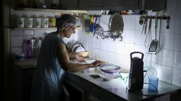 Samira Hanna, 70, washes dishes in her kitchen as she uses a portable electric light due to a power cut, in Beirut. (Reuters)