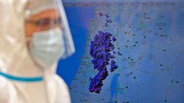A doctor, from the Palestinian Ministry of Health, stands next to a map tracking the location of people infected with the novel coronavirus COVID-19 in Hebron in the occupied West Bank on July 15, 2020. (AFP)
