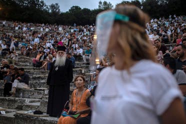 A steward wearing plastic visor stands in front of a Greek Orthodox priest as spectators take their seats at the ancient theater of Epidaurus, Greece. (AP)