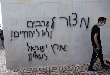 A Palestinian man walks by a wall spray painted with anti-Palestinian slogans in Hebrew that read, a siege on the Arabs, not on the Jews, the land of Israel is for Israelis, at a mosque in el-Bireh, near the West Bank city of Ramallah, Monday, July 27, 2020. (AP)