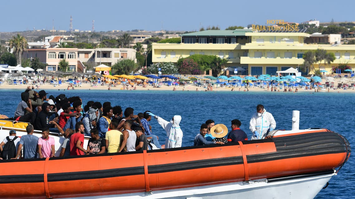 Migrants from Tunisia and Lybia are examined as they arrive onboard of an Italian Guardia Costiera (Coast Guard) boat in the Italian Pelagie Island of Lampedusa, while a beach with tourists is seen in the background, on August 1, 2020.