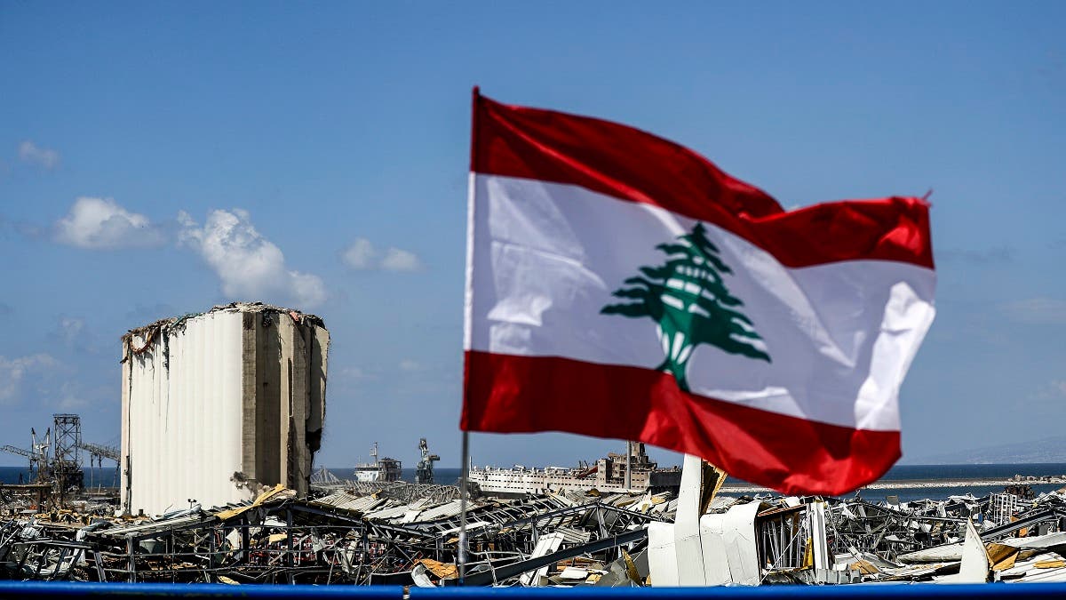 This picture taken on August 9, 2020 shows a Lebanese flag flying along a bridge near the port of Lebanon's capital Beirut, while in the background are seen the damaged grain silos opposite the blast site of a colossal explosion due to a huge pile of ammonium nitrate that had languished for years at a port warehouse. (AFP)