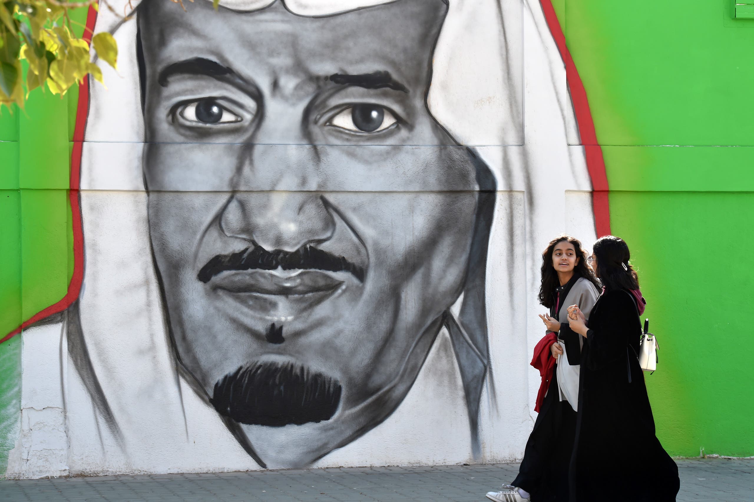 Saudi women walk past a mural painting showing King Salman bin Abdulaziz on Tahliya street in the capital Riyadh on December 5, 2019. (AFP)