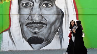 Saudi women walk past a mural painting showing King Salman bin Abdulaziz on Tahliya street in the capital Riyadh on December 5, 2019. (AFP)