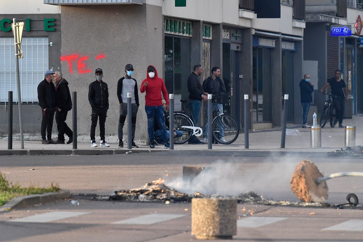 People stand near a torn down street sign and a fire in the street in the Gresilles area of Dijon, eastern France, on June 15, 2020. (AFP)