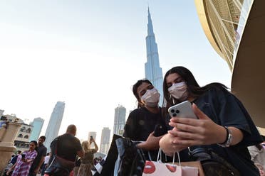 Women wearing protective masks look at a cell phone in front of Burj Khalifa in Dubai on March 8, 2020. (AFP)