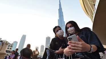 Women wearing protective masks look at a cell phone in front of Burj Khalifa in Dubai on March 8, 2020. (AFP)