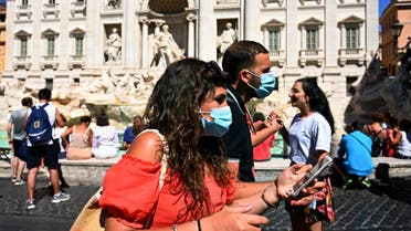 Tourists wearing a surgical face mask walk by the Trevi fountain in downtown Rome on August 19, 2020. (AFP)