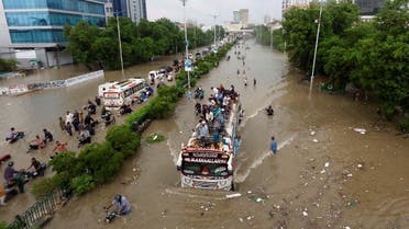 People sit atop a bus roof while others wade through the flooded road during monsoon rain in Karachi. (Reuters)