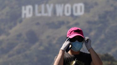 A person wearing a face mask and gloves adjusts glasses while taking photos of the Hollywood sign in Los Angeles, California, U.S., May 9, 2020. (Reuters)
