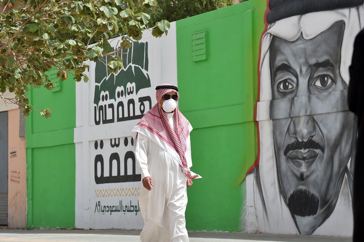 A Saudi man, wearing a protective mask as a precaution against COVID-19 coronavirus disease, walks past a mural showing the face of King Salman bin Abdulaziz. (File photo: AFP)