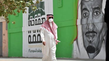 A Saudi man, wearing a protective mask as a precaution against COVID-19 coronavirus disease, walks past a mural showing the face of King Salman bin Abdulaziz. (File photo: AFP)