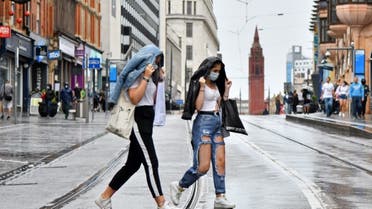 Two women wearing protective face masks cross tram tracks in the rain in Birmingham, central England on August 22, 2020. (AFP)