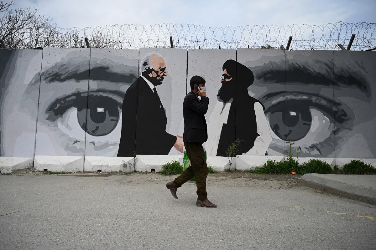 A man wearing a facemask as a precautionary measure against the COVID-19 novel coronavirus walk past a wall painted with images of US Special Representative for Afghanistan Reconciliation Zalmay Khalilzad (L) and Taliban co-founder Mullah Abdul Ghani Baradar (R), in Kabul. (AFP)