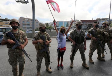 A demonstrator raises a Lebanese flag while standing between soldiers, during a protest against the government's performance and worsening economic conditions, near the presidential palace in Baabda, Lebanon June 25, 2020. (Reuters)