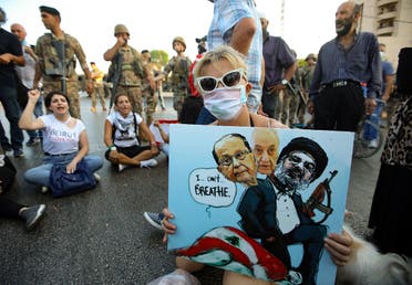 A Lebanese anti government protester holds a placard with a cartoon of (L-R) President Michel Aoun, Parliament Speaker Nabih Berri and head of the Shiite movement Hezbollah Hassan Nasrallah sitting atop a national flag (with writing that refers to George Floyd's death) during a demonstration against the lack of progress in a probe by authorities into a monster blast that ravaged swathes of the capital 40 days ago, near the presidential palace in Baabda. (AFP)