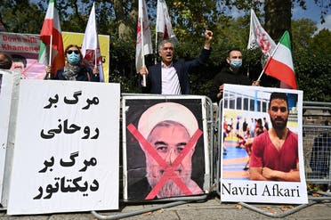 Protesters wave the Lion and Sun flag of the National Council of Resistance of Iran and the white flag of the People's Mujahedin of Iran, two Iranian opposition groups, with a placard depicting the crossed out face of Iran's President Hassan Rouhani as they demonstrate outside the Iranian embassy in London on September 12, 2020 against the execution of Iranian wrestler Navid Afkari. (AFP)
