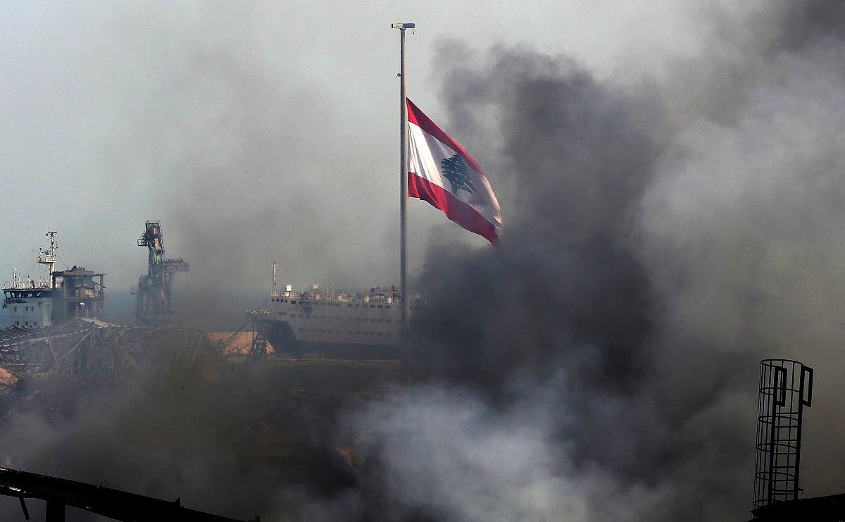 A Lebanese flag flutters amid billowing smoke as firefighters (unseen) extinguish the remaining flames at the seaport of Beirut, on September 11, 2020, a day after a huge fire erupted in harbour warehouses. (AFP)