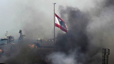 A Lebanese flag flutters amid billowing smoke as firefighters (unseen) extinguish the remaining flames at the seaport of Beirut, on September 11, 2020, a day after a huge fire erupted in harbour warehouses. (AFP)