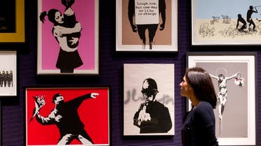 A gallery assistant poses for a picture with part of a collection of 30 Banksy prints, including the well-known 'Rage, Flower Thrower' (bottom L), owned by the British gallery owner, Steve Lazarides, at Bonhams auction house in London on Janurary 23, 2015. (AFP)