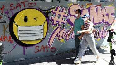 People wearing face masks walk past a graffito depicting a smiley face with a face mask in Ankara, on September 7, 2020, amid the coronavirus pandemic. (AFP)