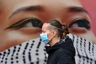 A pedestrian wearing a face mask as a precaution against the transmission of the novel coronavirus, walks past a poster of a person wearing a face covering, in the high street in west London on October 11, 2020. (AFP)
