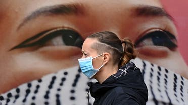 A pedestrian wearing a face mask as a precaution against the transmission of the novel coronavirus, walks past a poster of a person wearing a face covering. (File photo: AFP)