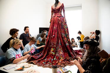 A group of women add small embroidery pieces to the hem at a pop-up exhibition in Bristol, UK, on International Women's Day. (Supplied: Mireya Gonzales)