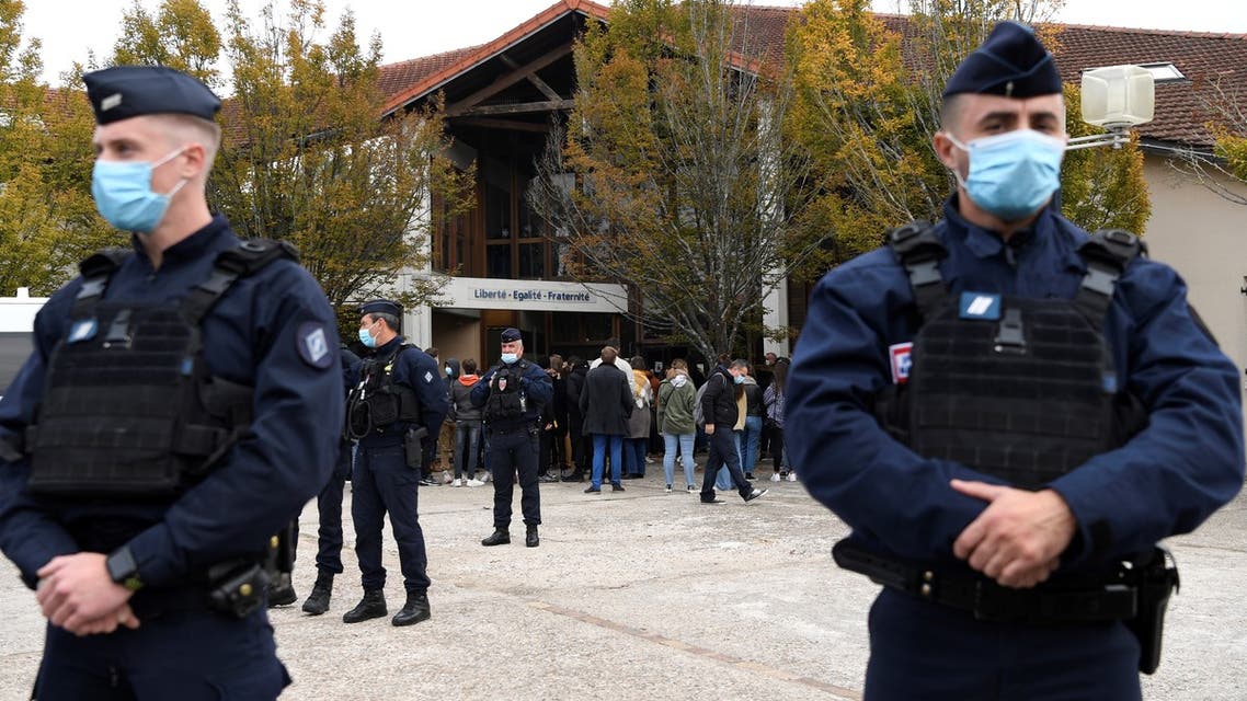 French police officers stand as adults and children gather in front of flowers displayed at the entrance of a middle school in Conflans-Sainte-Honorine, 30kms northwest of Paris, on October 17, 2020, after a teacher was decapitated by an attacker who has been shot dead by policemen. The man suspected of beheading on October 16 ,2020 a French teacher who had shown his students cartoons of the prophet Mohammed was an 18-year-old born in Moscow and originating from Russia's southern region of Chechnya, a judicial source said on October 17. Five more people have been detained over the murder on October 16 ,2020 outside Paris, including the parents of a child at the school where the teacher was working, bringing to nine the total number currently under arrest, said the source, who asked not to be named. The attack happened at around 5 pm (1500 GMT) near a school in Conflans Saint-Honorine, a western suburb of the French capital. The man who was decapitated was a history teacher who had recently shown caricatures of the Prophet Mohammed in class.