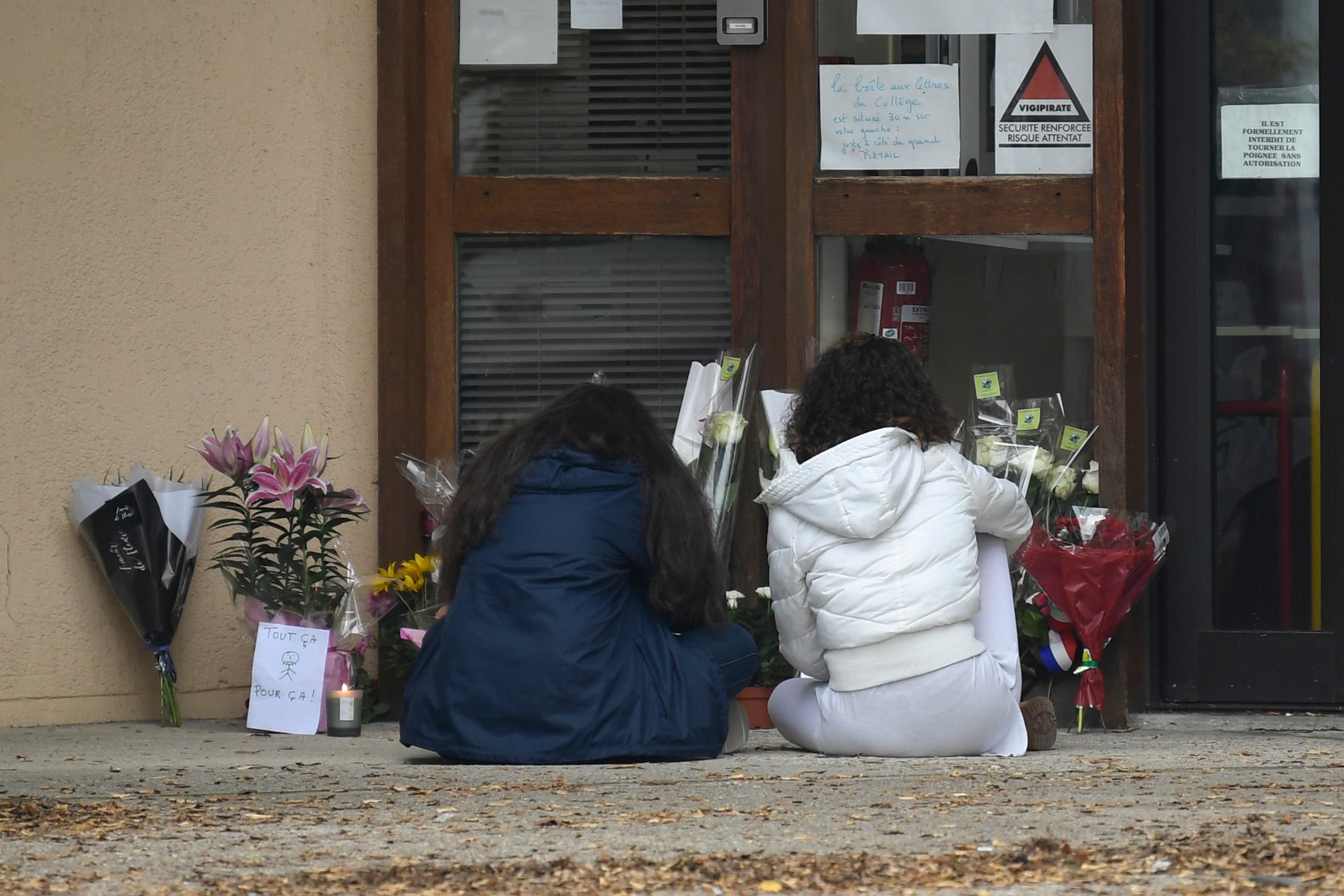 طفلتان تضعان الورود أمام مدخل المدرسة حيث كان يدرِّس باتي
