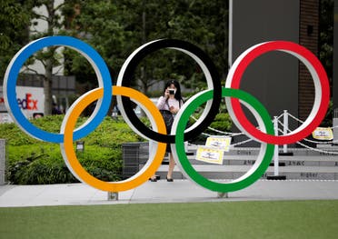 A woman wearing a protective mask amid the coronavirus disease (COVID-19) outbreak, takes a picture of the Olympic rings in front of the National Stadium in Tokyo, Japan October 14, 2020. 