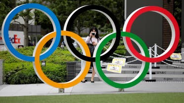 A woman wearing a protective mask amid the coronavirus disease (COVID-19) outbreak, takes a picture of the Olympic rings in front of the National Stadium in Tokyo, Japan October 14, 2020. REUTERS