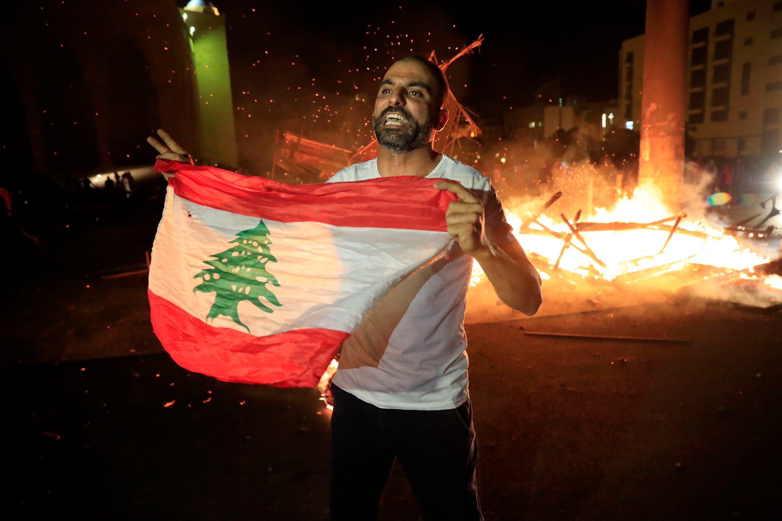A protester holds the Lebanese flag and shouts slogans denouncing the naming of former Lebanese Prime Minister Saad Hariri as a potential candidate for prime minister, after Hariri's supporters burned a significant protest symbol erected in downtown Beirut on Oct. 21, 2020. (AP)