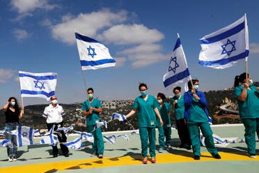 Medical staff hold Israeli national flags before a fly over by the Israeli Air Force over Hadassah Ein Kerem hospital in Jerusalem on April 29, 2020. (Reuters)