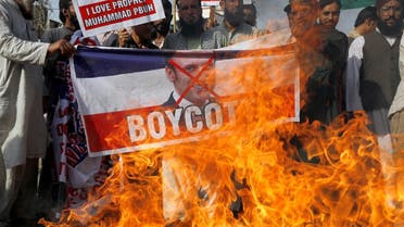 People chant slogans as they set fire to a banner with a crossed-out image of French President Emmanuel Macron during a protest against cartoon publications of Prophet Mohammad in France and Macron's comments, in Karachi, Pakistan. (Reuters)