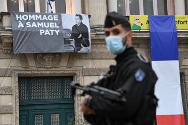 A French police officer stands next to a portrait of French teacher Samuel Paty on display on the facade of the Opera Comedie in Montpellier on October 21, 2020. (AFP)